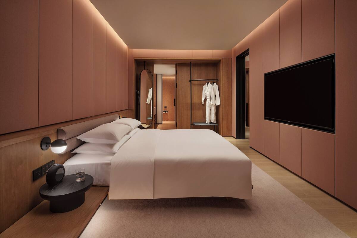 A modern hotel room with a large bed, bedside table, and a TV mounted on the wall.