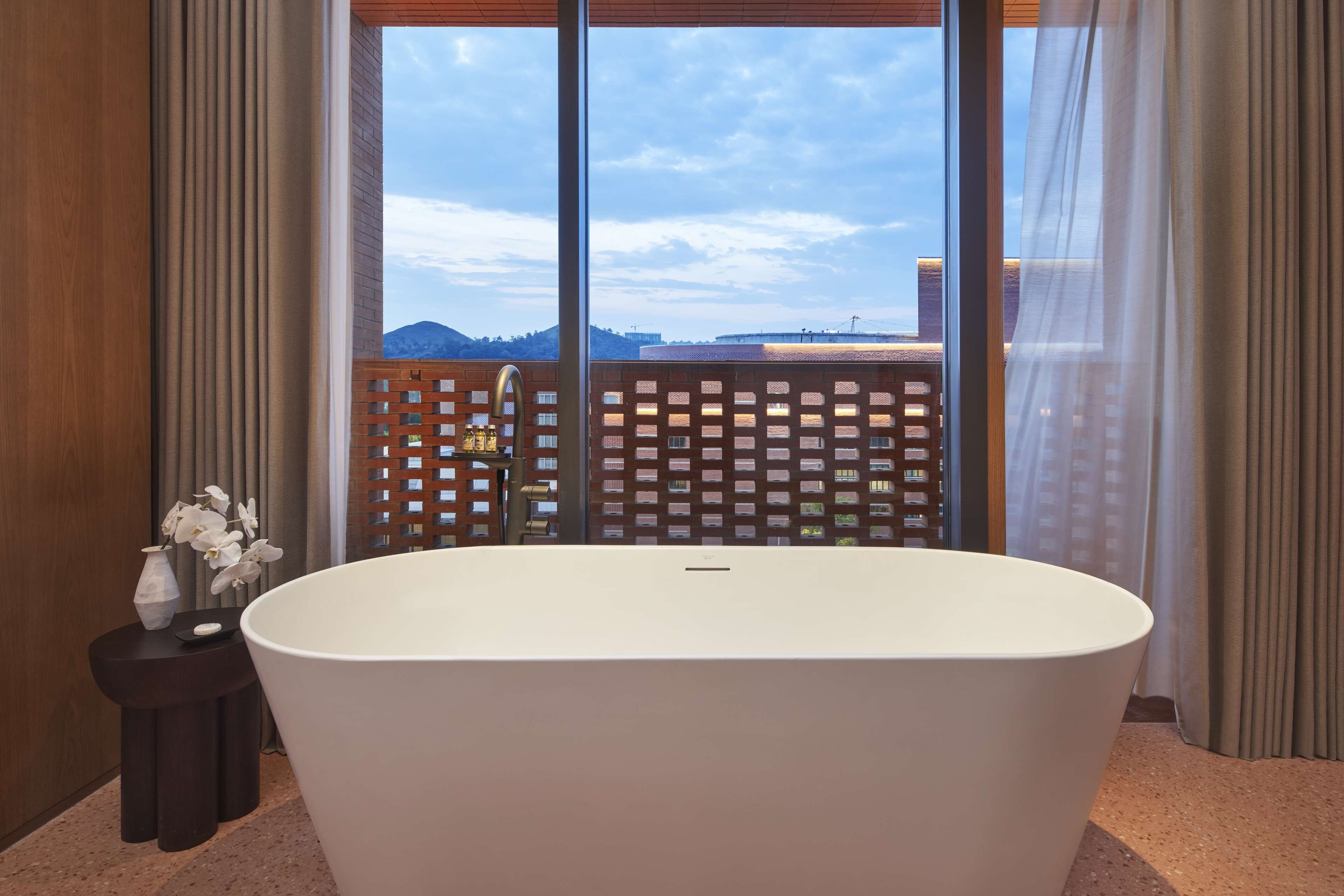 Un baño moderno con una bañera independiente, ventanas amplias y vistas a un paisaje urbano.