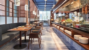 A modern restaurant with wooden tables and chairs, a buffet area, and a brick wall with large windows.