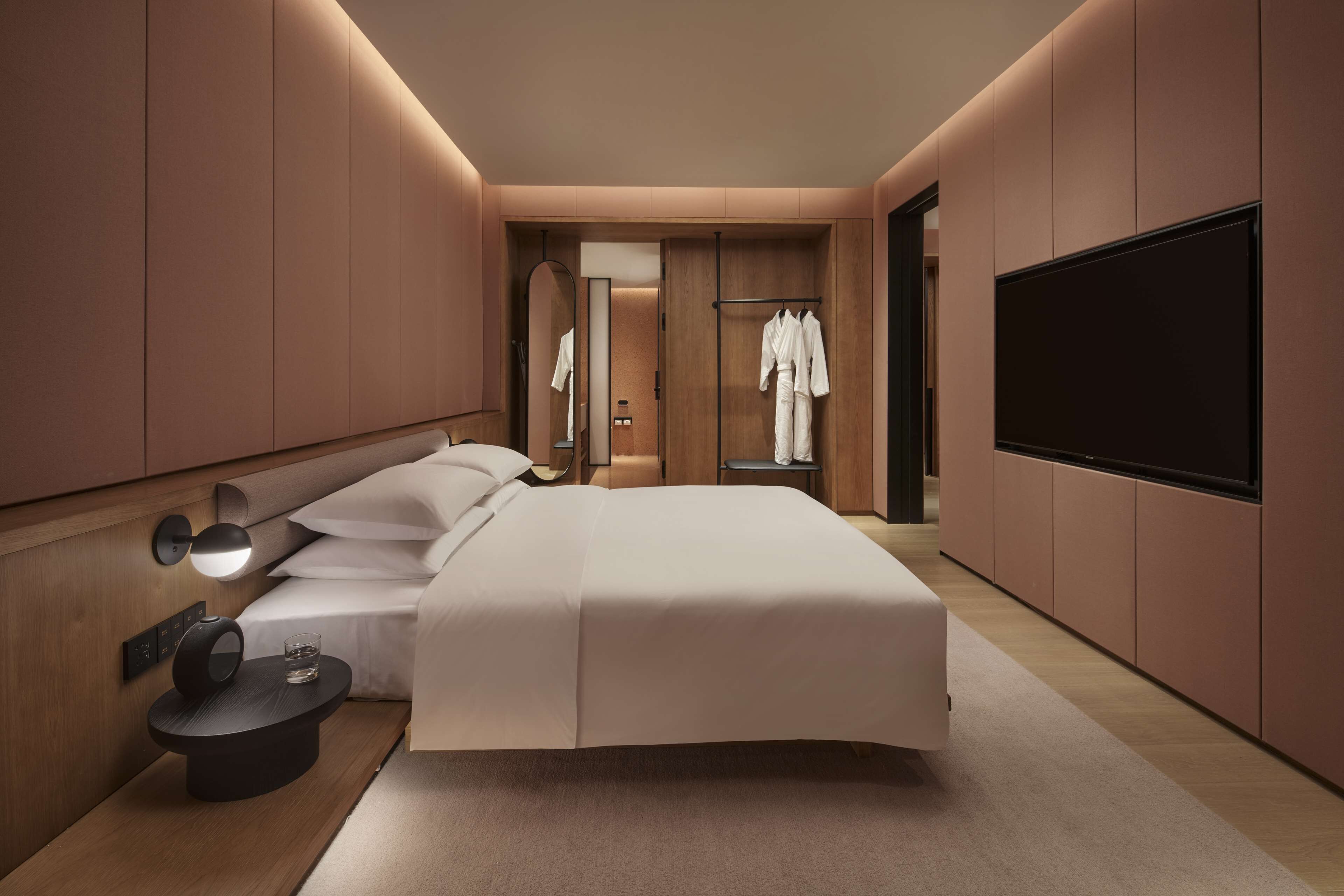 Una habitación de hotel moderna con una cama grande, mesitas de noche, un televisor de pantalla plana y un vestidor.