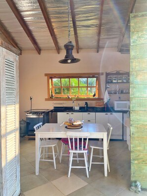 A kitchen with a dining table, chairs, a window with a view of greenery, a stove, and a microwave. - Casa Alto do Vale: The most beautiful view of the mountains. (Araras)