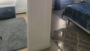 Een slaapkamer met een bed, nachtkastje, lamp, raam met zonwering, en een deur.