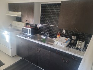 A kitchen with dark cabinets, a microwave, a toaster, and a sink.