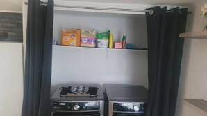 Een wasruimte met twee wasmachines en een plank met schoonmaakmiddelen.