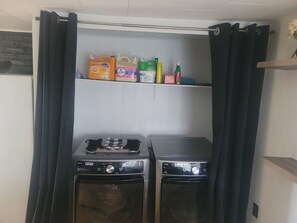 A laundry area with two washing machines and a shelf with cleaning supplies.