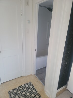 A room with a white door, a patterned rug, and a black brick wall.