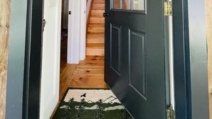 Un pasillo que lleva a una escalera con una puerta negra y un aplique decorativo encima.