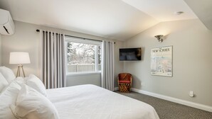 Ein Hotelzimmer mit einem großen Bett, einem Sessel, einem Fernseher und einem Fenster mit Vorhängen.