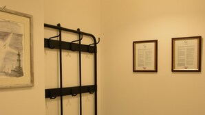 Ein Flur mit einer schwarzen Metallbank, einem an der Wand befestigten Ablagegestell und zwei gerahmten Zertifikaten.