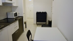 Eine kleine Küchenzeile mit Mikrowelle, Spüle und Schrank. Es gibt einen Tisch mit einem Stuhl, eine kleine Bank und einen Wäscheständer mit aufgehängten Gegenständen.