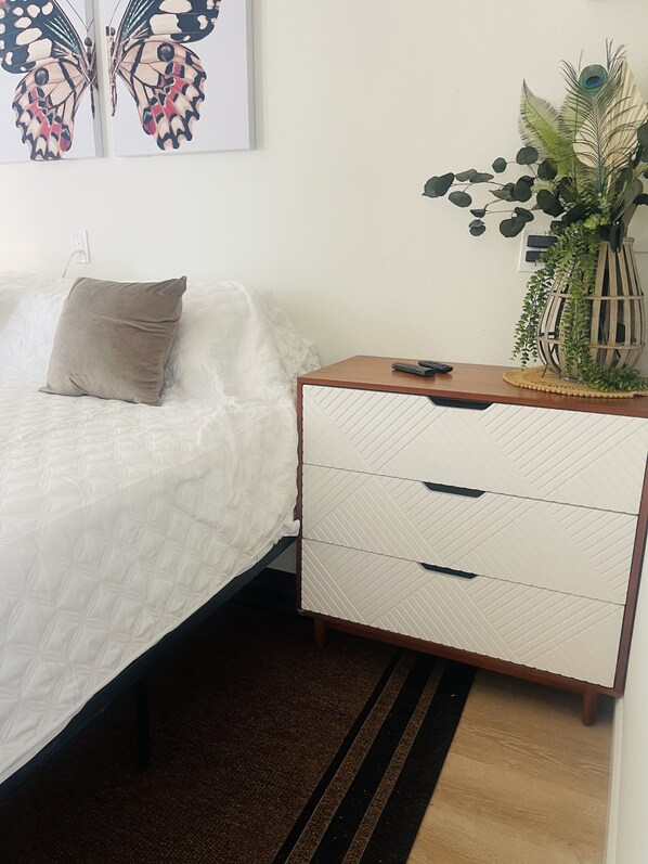 A neatly made bed with a pillow, a bedside table with a remote control, and a decorative plant.