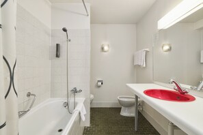 A bathroom with a white bathtub, a red sink, a toilet, and a shower. - Neuchatel City Hotel (Neuchatel)