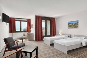 A hotel room with two beds, a desk, a chair, a TV, and a view of the city. - Neuchatel City Hotel (Neuchatel)