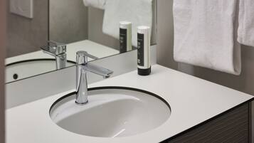 A modern bathroom with a white sink, chrome faucet, and a mirror reflecting a towel and toiletries.