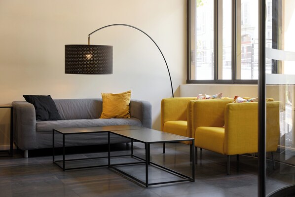 Una sala de estar moderna con un sofá gris, una mesa de centro negra, un sillón amarillo y una lámpara de pie.