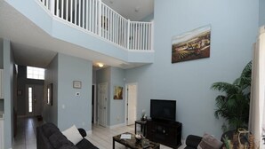 A spacious living room with a high ceiling and a balcony, furnished with black sofas and a coffee table. - Terra Verde 116 (Kissimmee)