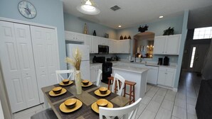 A modern kitchen with white cabinets, a central island, and a dining area with a table set for four. - Terra Verde 116 (Kissimmee)