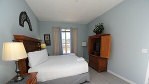 A bedroom with a large bed, a wooden dresser, a TV cabinet, and a lamp. - Terra Verde 116 (Kissimmee)