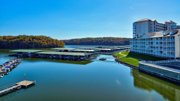 Een hotel aan het water met een jachthaven, een groot gebouw met meerdere balkons en een bebost heuvel op de achtergrond.