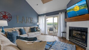 Een woonkamer met een bank, een open haard, een televisie en uitzicht op een meer.