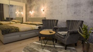A modern bedroom with a large bed, two armchairs, a small round table, and a mirror.