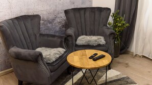 Two armchairs with fur throw pillows, a round wooden table with two remotes, and a potted plant.