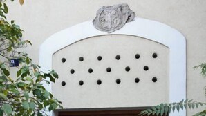 A traditional Japanese gate with a wooden door and a decorative stone plaque above it.