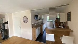 A modern kitchen with a central island, a dining area with a table and chairs, and a large clock on the wall. - Cozy house with garden and terrace (Espelkamp)