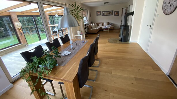 A modern dining area with a wooden table, chairs, and a hanging light fixture. - Cozy house with garden and terrace (Espelkamp)
