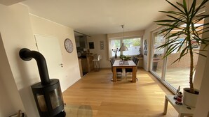 A modern kitchen with a wood-burning stove, a dining area with a wooden table and chairs, and a large window with a view of the outside. - Cozy house with garden and terrace (Espelkamp)