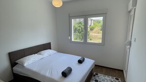 A bedroom with a bed, a window, a wooden floor, and a rug.