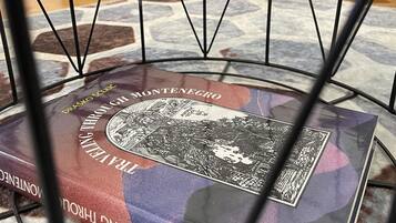 Un livre intitulé « Drasko à travers le Monténégro » est posé sur une table recouverte d’une nappe à motifs.