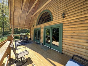Una cabaña de madera con porche cubierto, mobiliario exterior y vistas del bosque circundante.