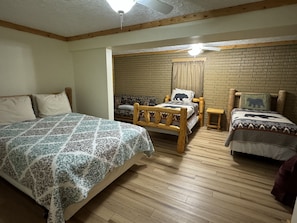 A cozy room with a large bed, a wooden chair, and a smaller bed with a bear-themed pillow.