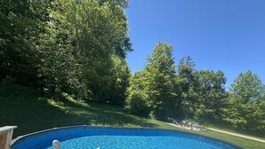Una piscina fuori terra con un pontile in legno, circondata da rigogliosi alberi verdi.