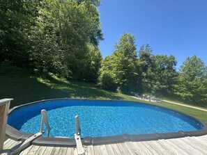 Ein oberirdischer Pool mit Holzterrasse, umgeben von üppigem Grün.