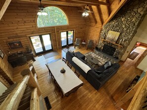 A log cabin interior with a stone fireplace, wooden furniture, and a large arched window. - Secluded Luxury Lodge 57 acres Hocking Hills Ohio (Logan)