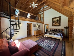 A spacious loft-style room with a high ceiling, a wooden staircase, a bed with a patterned bedspread, and a large window allowing natural light. - Secluded Luxury Lodge 57 acres Hocking Hills Ohio (Logan)