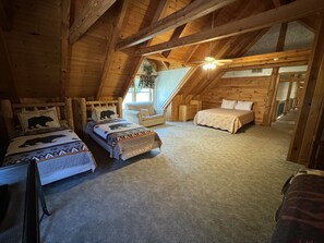 A cozy attic bedroom with two beds, a ceiling fan, and a large window.