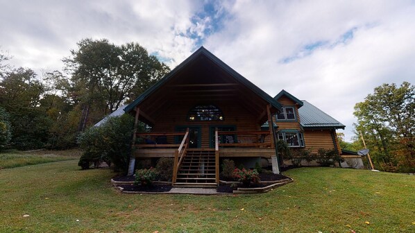Une cabane en rondins avec un porche à l’avant, un escalier menant à l’entrée et une antenne parabolique sur le toit.