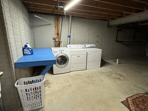 A laundry room with a washing machine and dryer, a blue table, and a laundry basket.