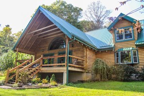 A log cabin with a large porch, a staircase, and a covered outdoor area.