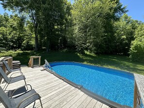 Une terrasse en bois avec une piscine, entourée d’une végétation luxuriante.