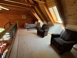 A cozy attic bedroom with a sloped ceiling, a bed, a patterned armchair, a sofa, and a small table with a lamp.