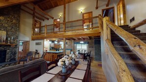 Un ambiente spazioso con soffitto alto, una zona pranzo con un tavolo lungo e una scala in legno.