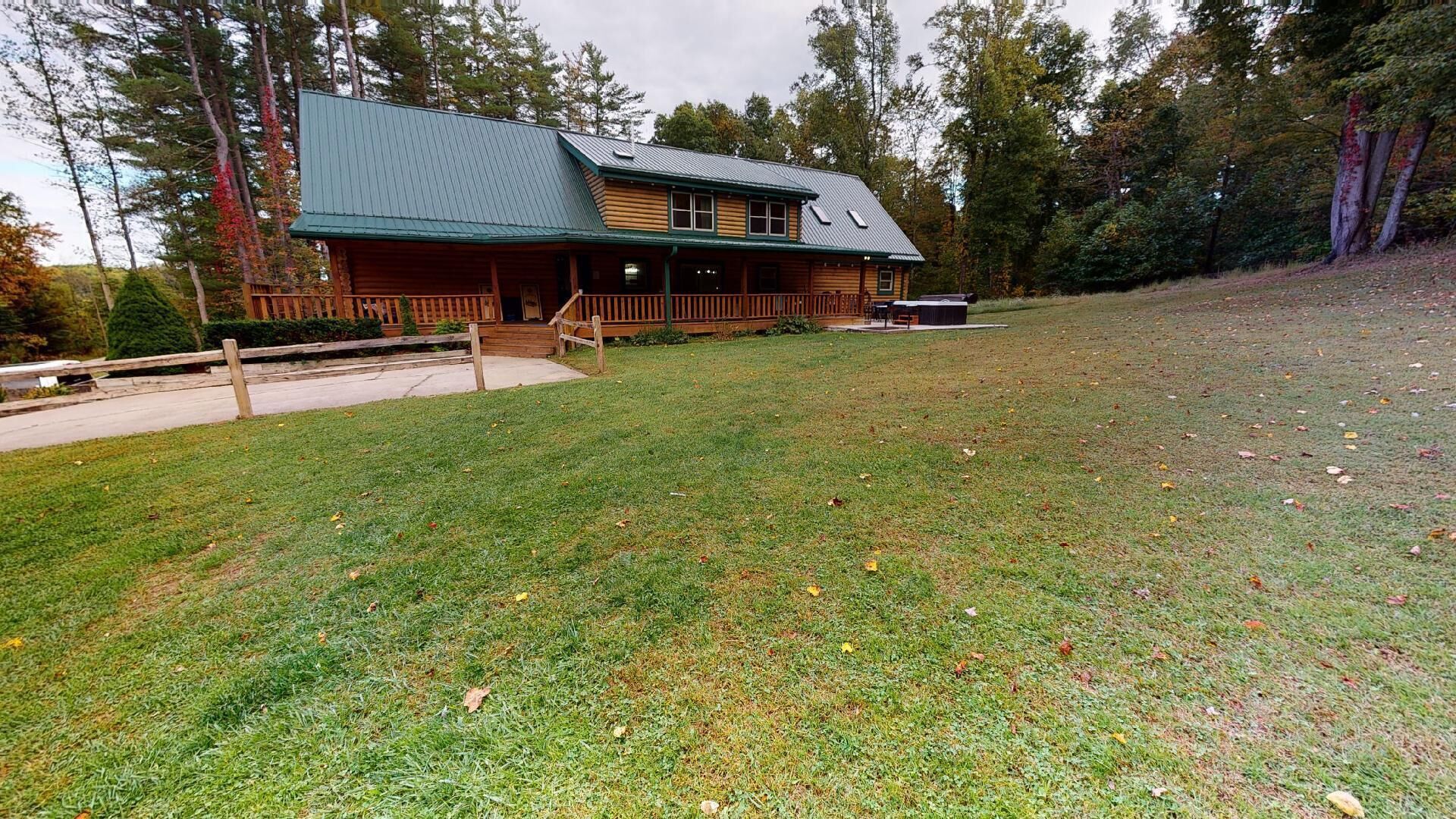 A log cabin with a green roof, a porch, and a covered outdoor seating area.