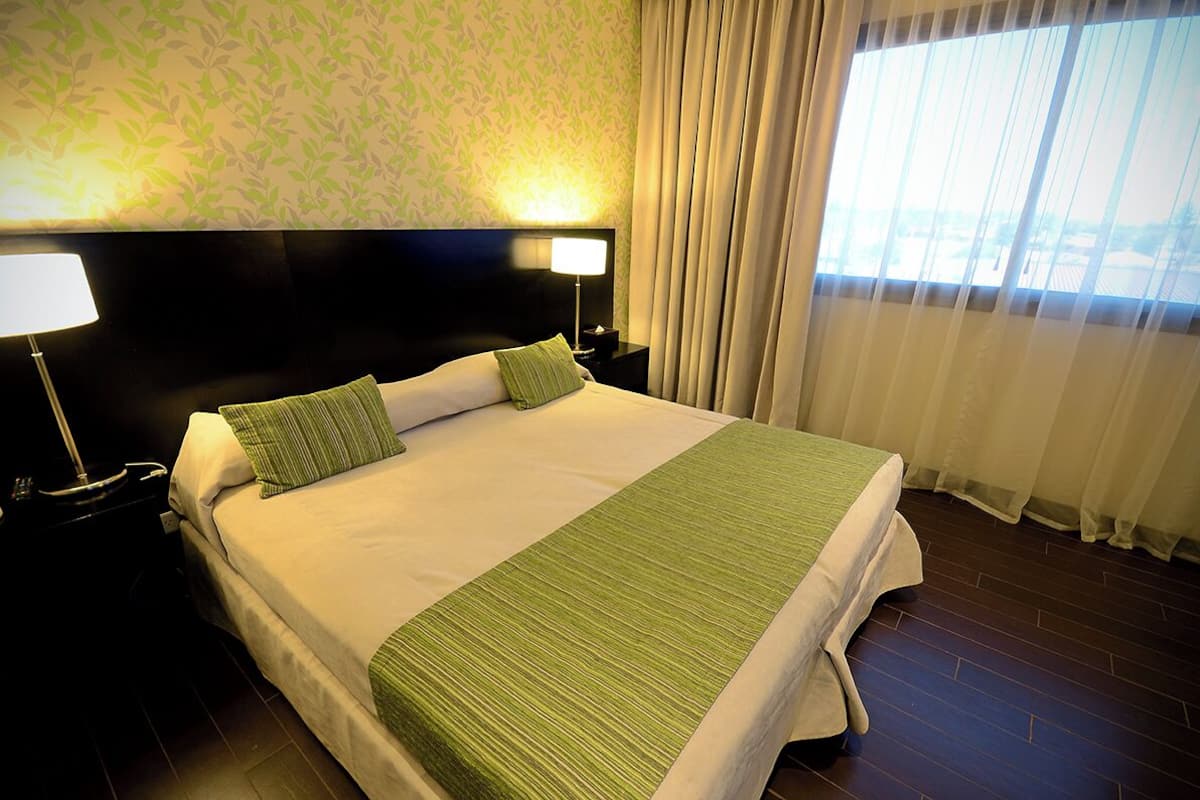 Un lit bien fait, avec une couvre-lit verte et des oreillers, une tête de lit noire et une table de chevet avec une lampe.
