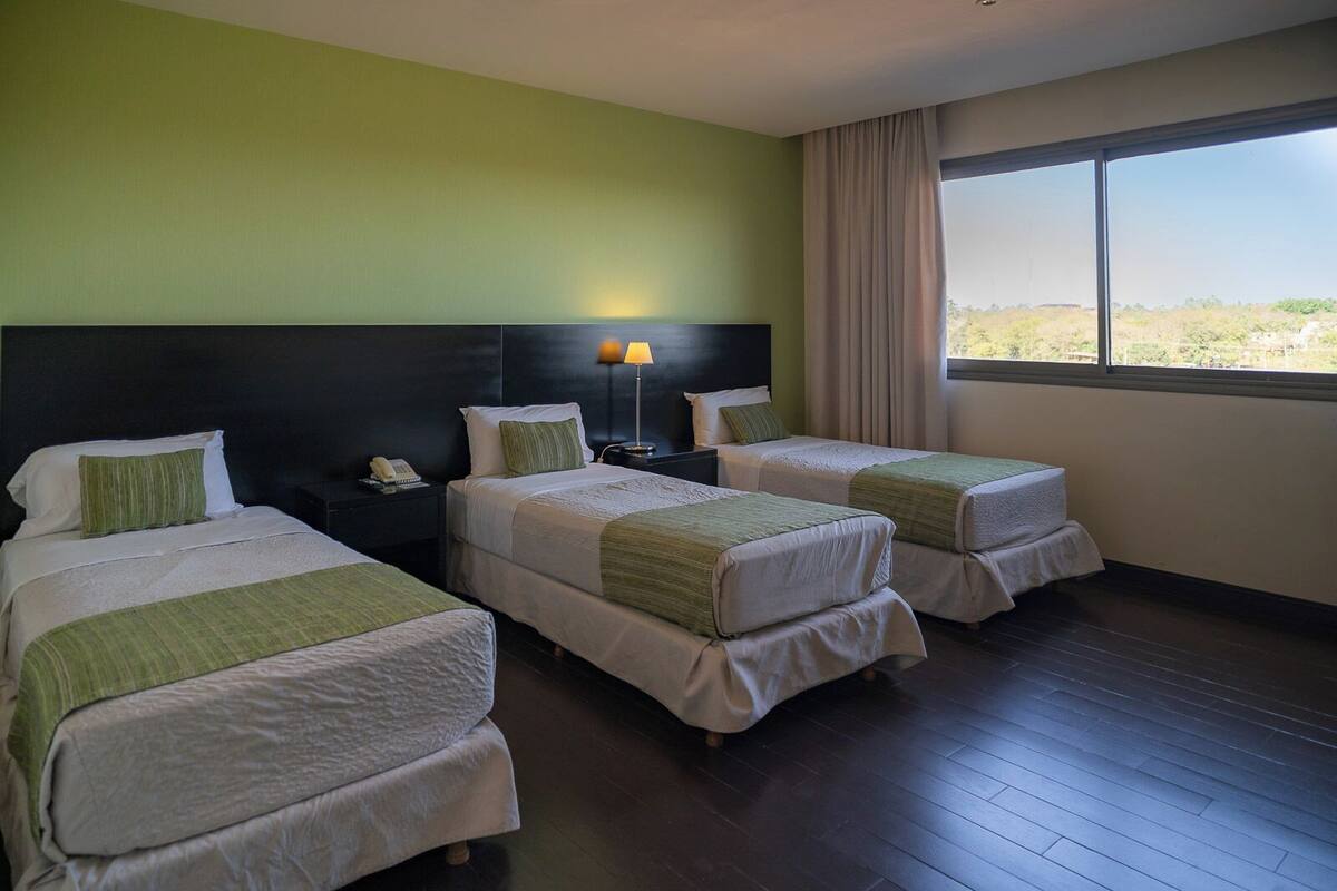 Une chambre d’hôtel avec deux lits, une table de chevet avec une lampe, un téléphone et une fenêtre donnant sur un beau paysage.