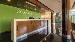 A reception desk at the Grand Crucero Iguazu Hotel with a green wall and a view of the hotel lobby.