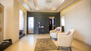 Una sala de estar moderna con una araña, sillones blancos, una alfombra y una pared decorativa oscura.
